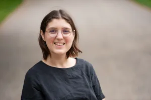 Porträt von Mechthild, einer Fweißen Frau mit schulterlangen hellbraunen Haaren. Sie trägt ein dunkelblaues T-Shirt und eine runde Brille.